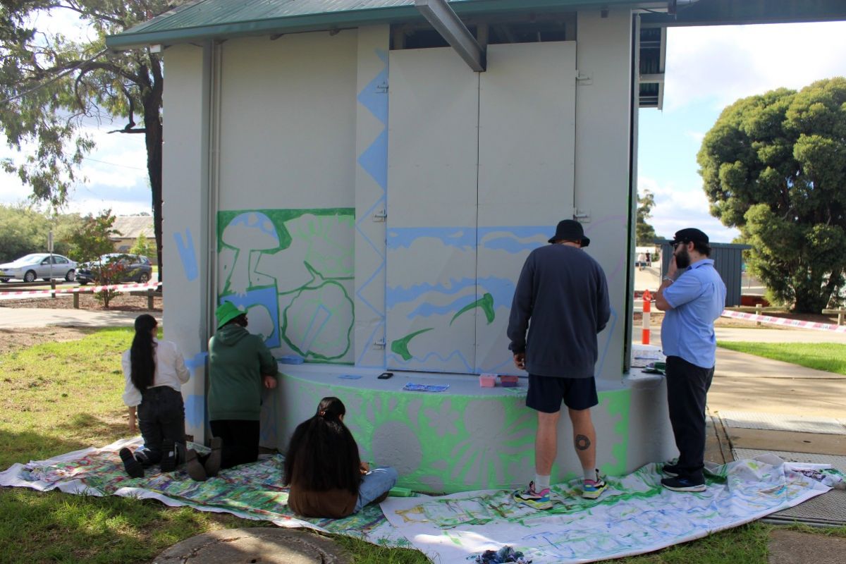 Mural being painted by three young people with artist giving guidance