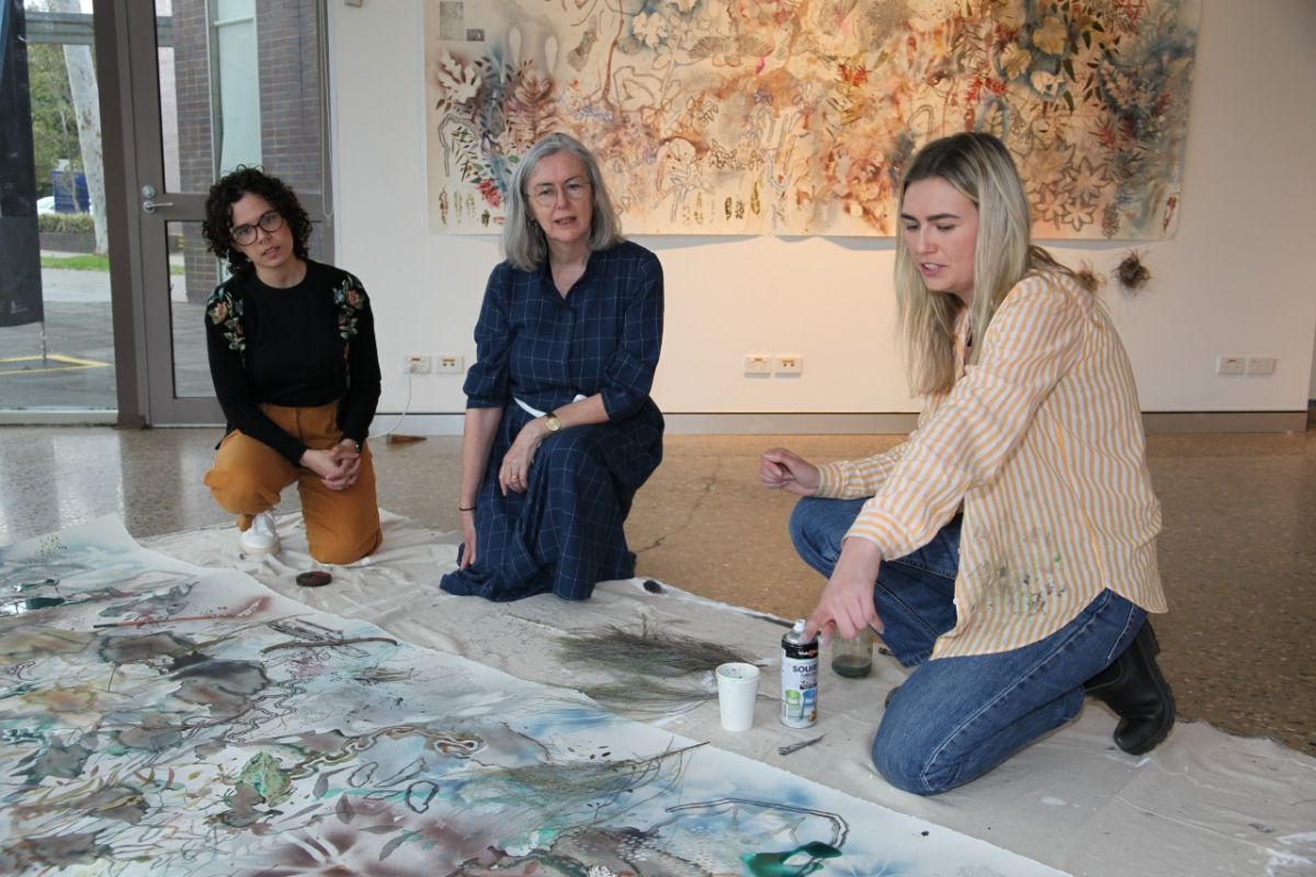 Three women crouching beside a large artwork on the floor