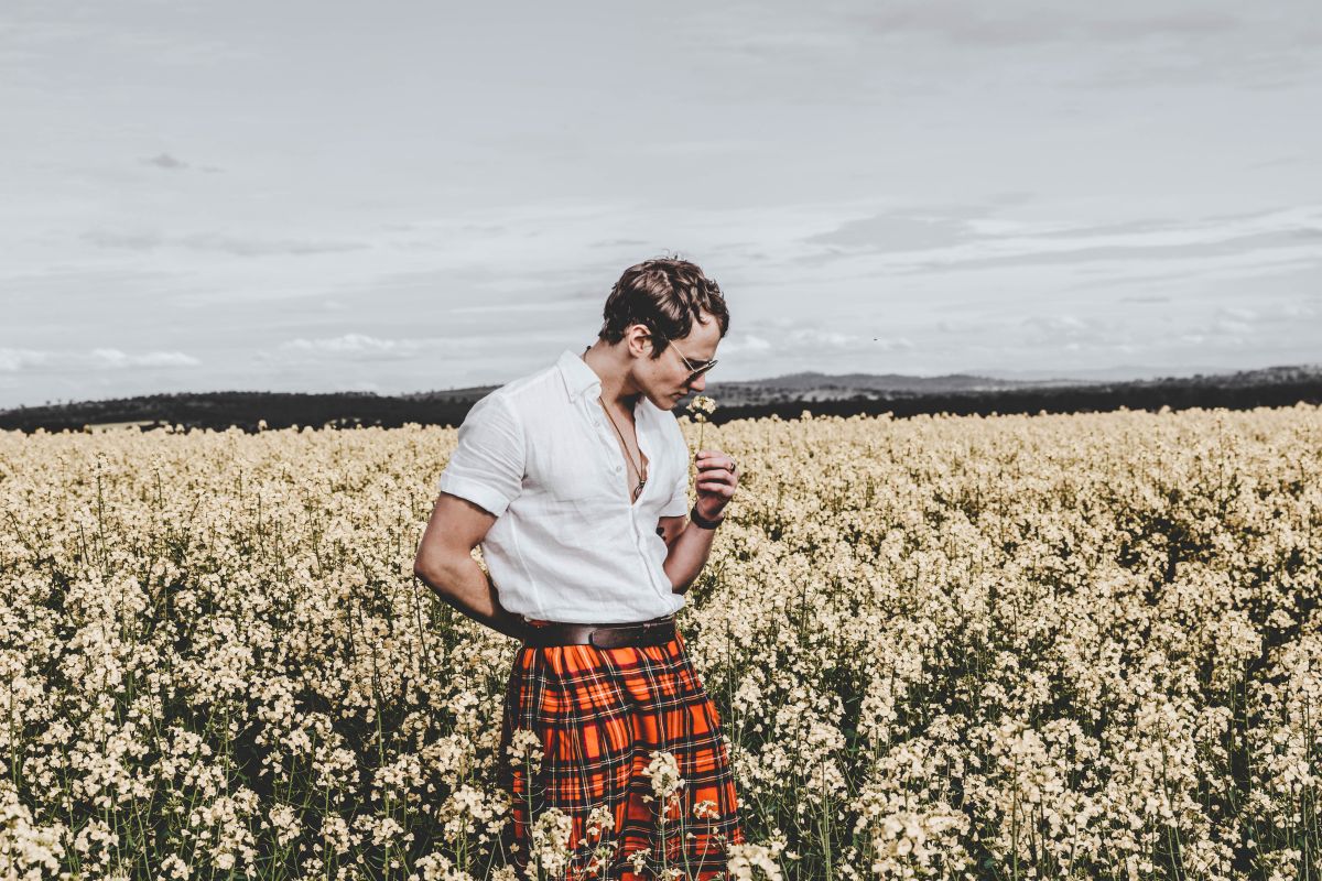 Man wearing kilt standing in field of flowers, smelling flower