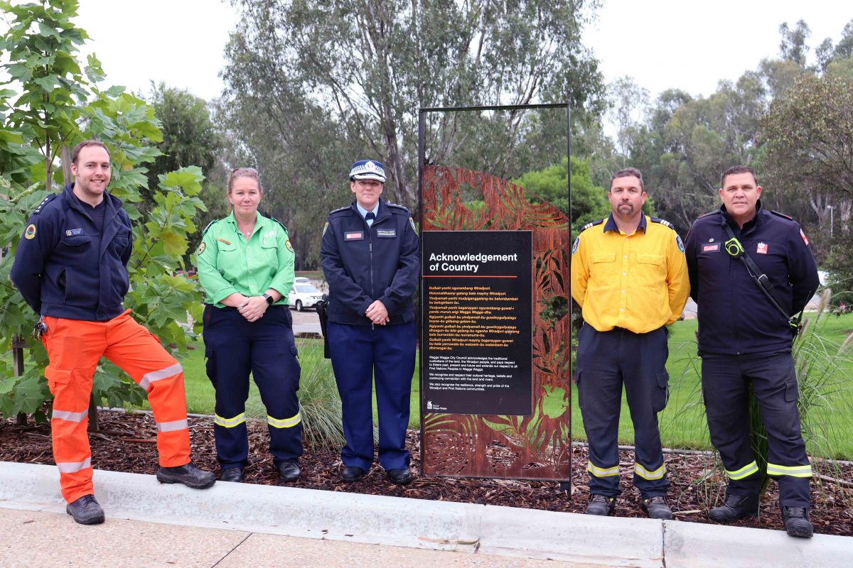 Representatives from SES, VRA, Police, RFS, Fire and Rescue standing beside Acknowledgement of Country sign