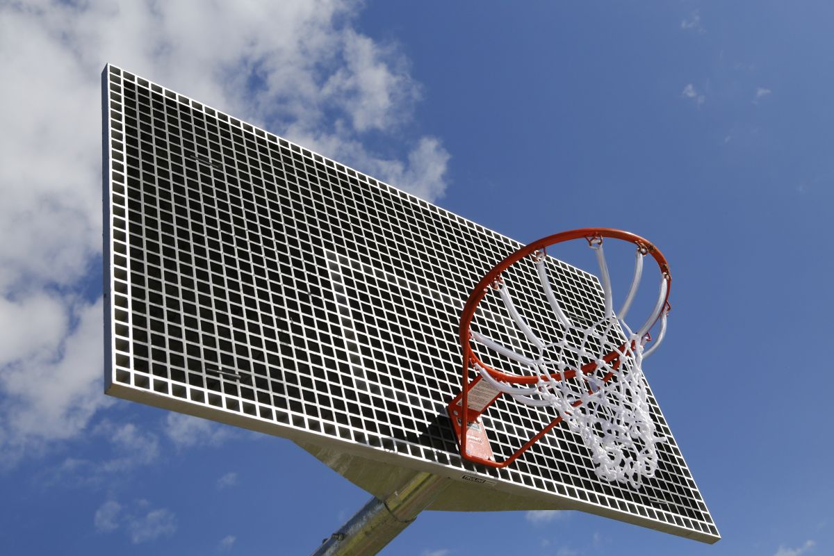 A basketball hoop viewed from below, blue sky and clouds behind it. 