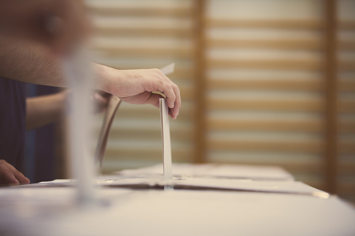 Hand placing a voting slip into a ballot box