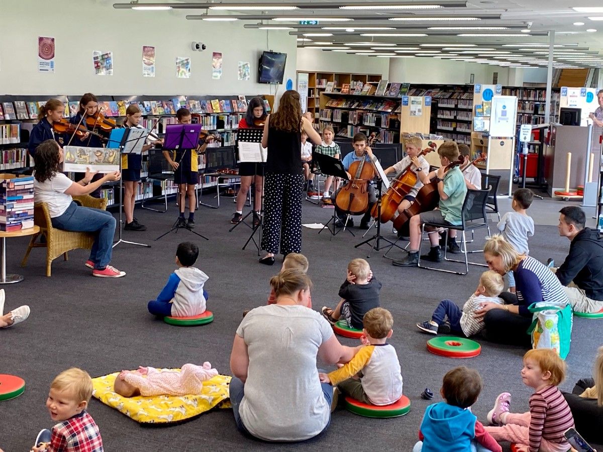 Children play instruments in library to audience of parents and toddlers