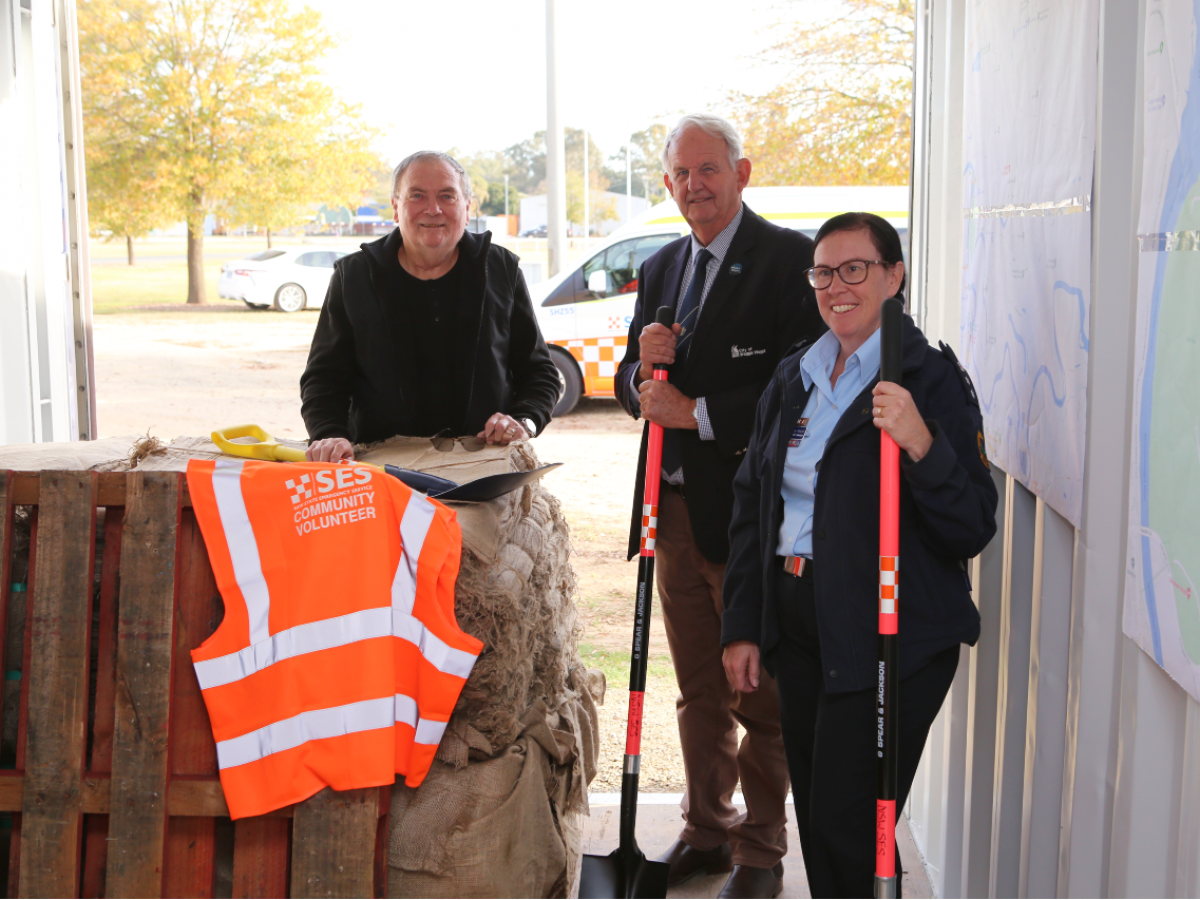 Three people standing beside a stack of hessian bags