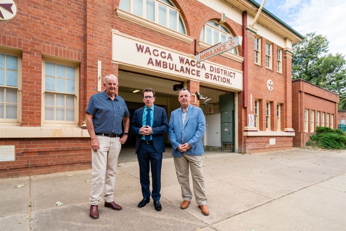 Three men stand in front of a historic former ambulance station