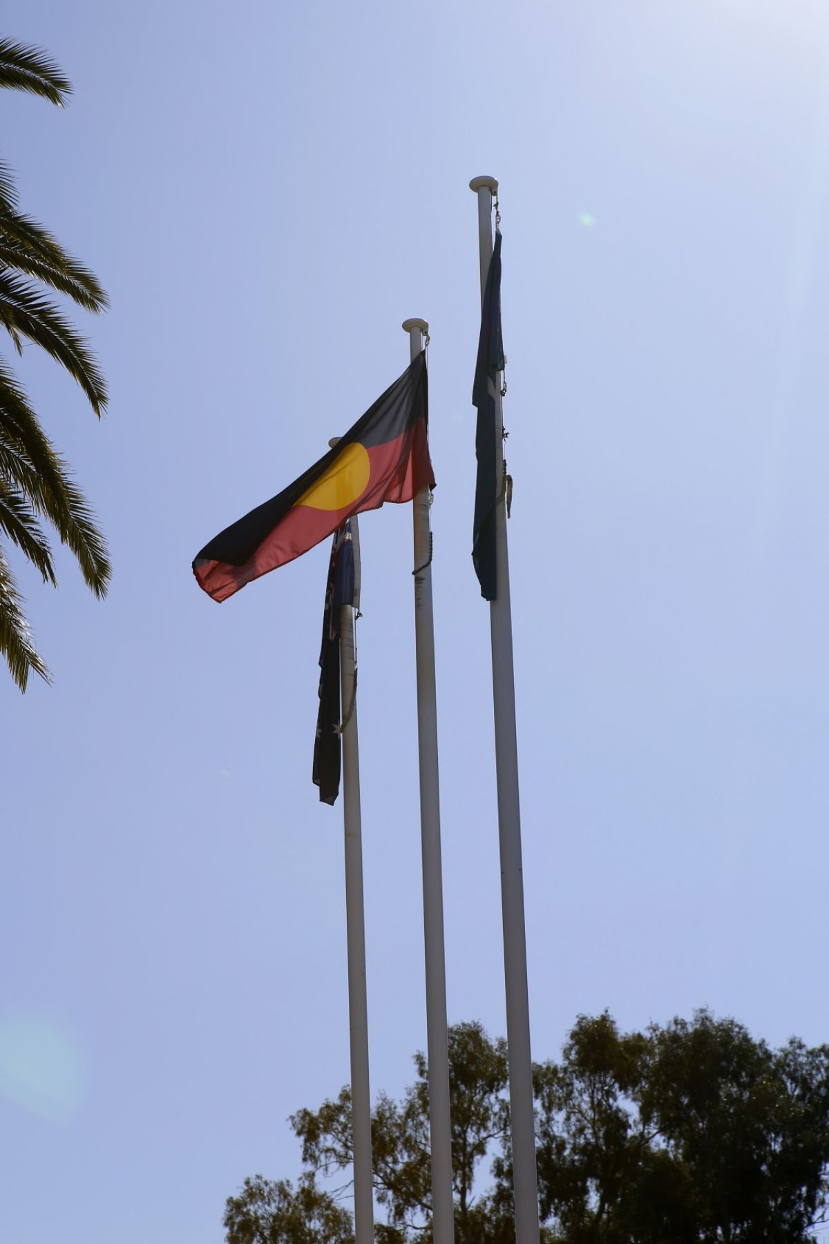 Australian, Aboriginal and Torres Strait Islander flags raised, against blue sky