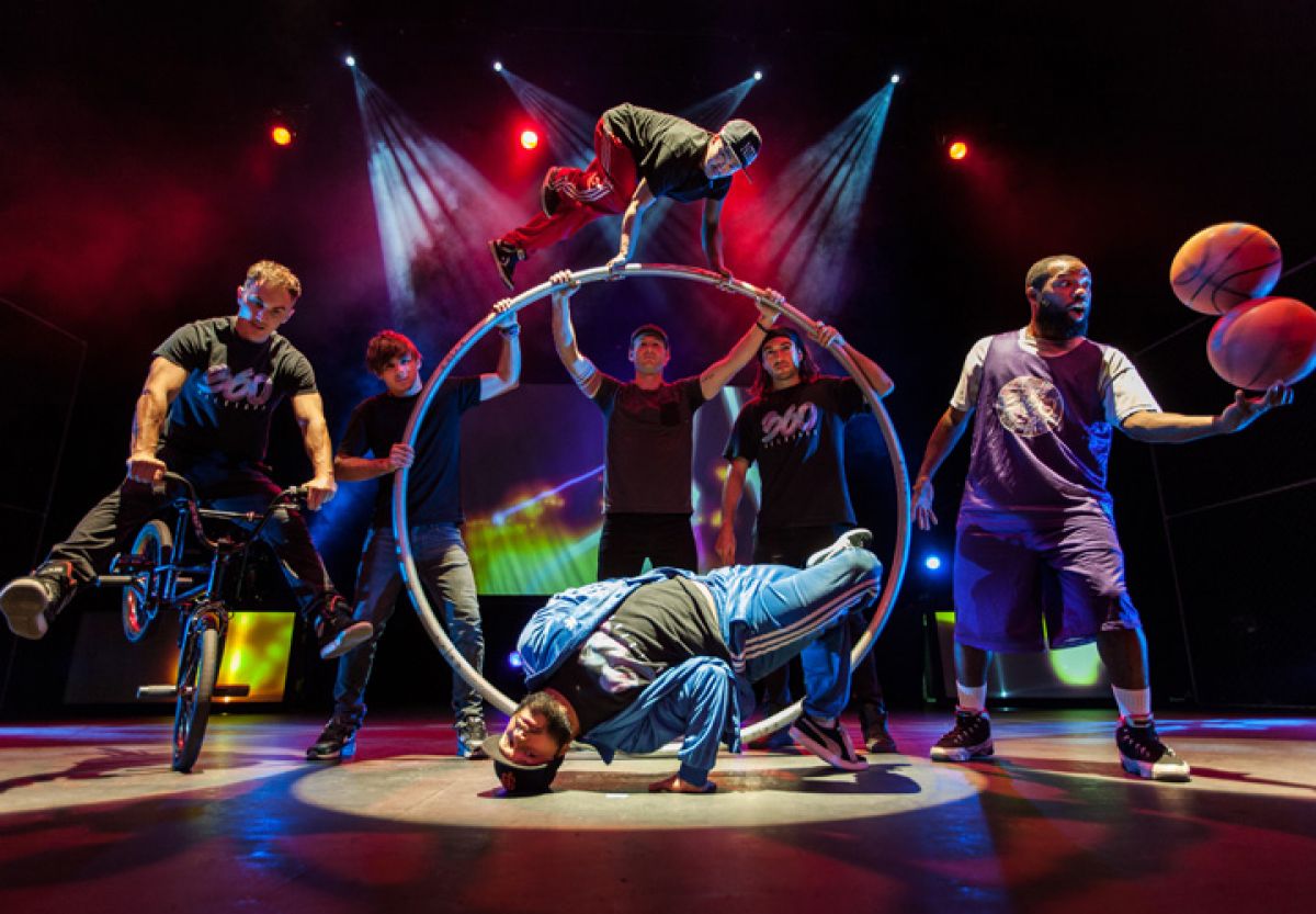 A group of men on a stage doing tricks with bikes, basketballs and large hoops