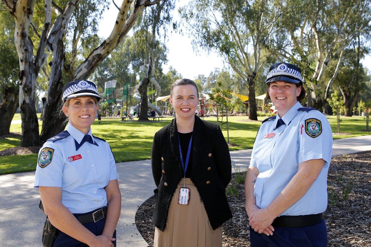 Two female police inspectors and woman standing with Riverside playground in background