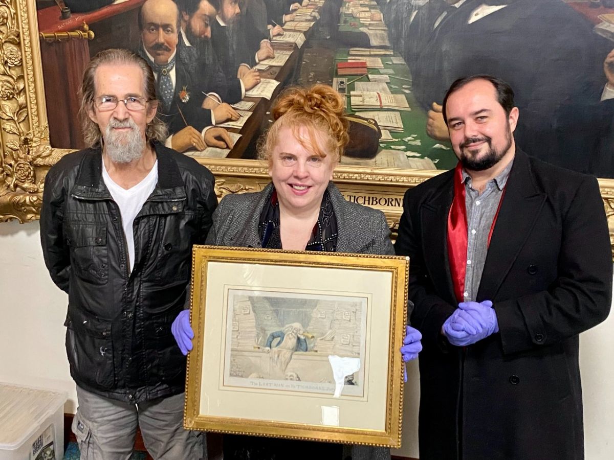 Two men and a woman, who is holding a small watercolour artwork