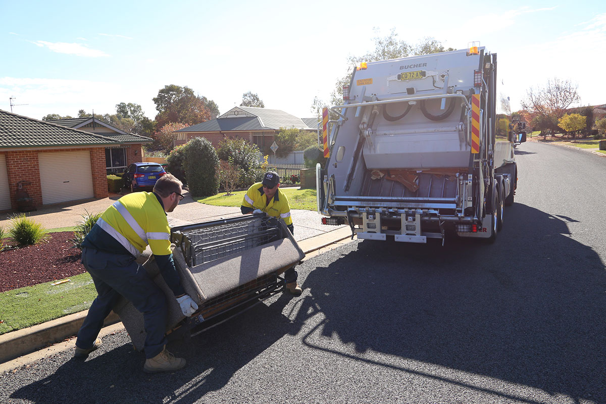 Two council employees picking up an old lounge chair for a hardwaste pickup