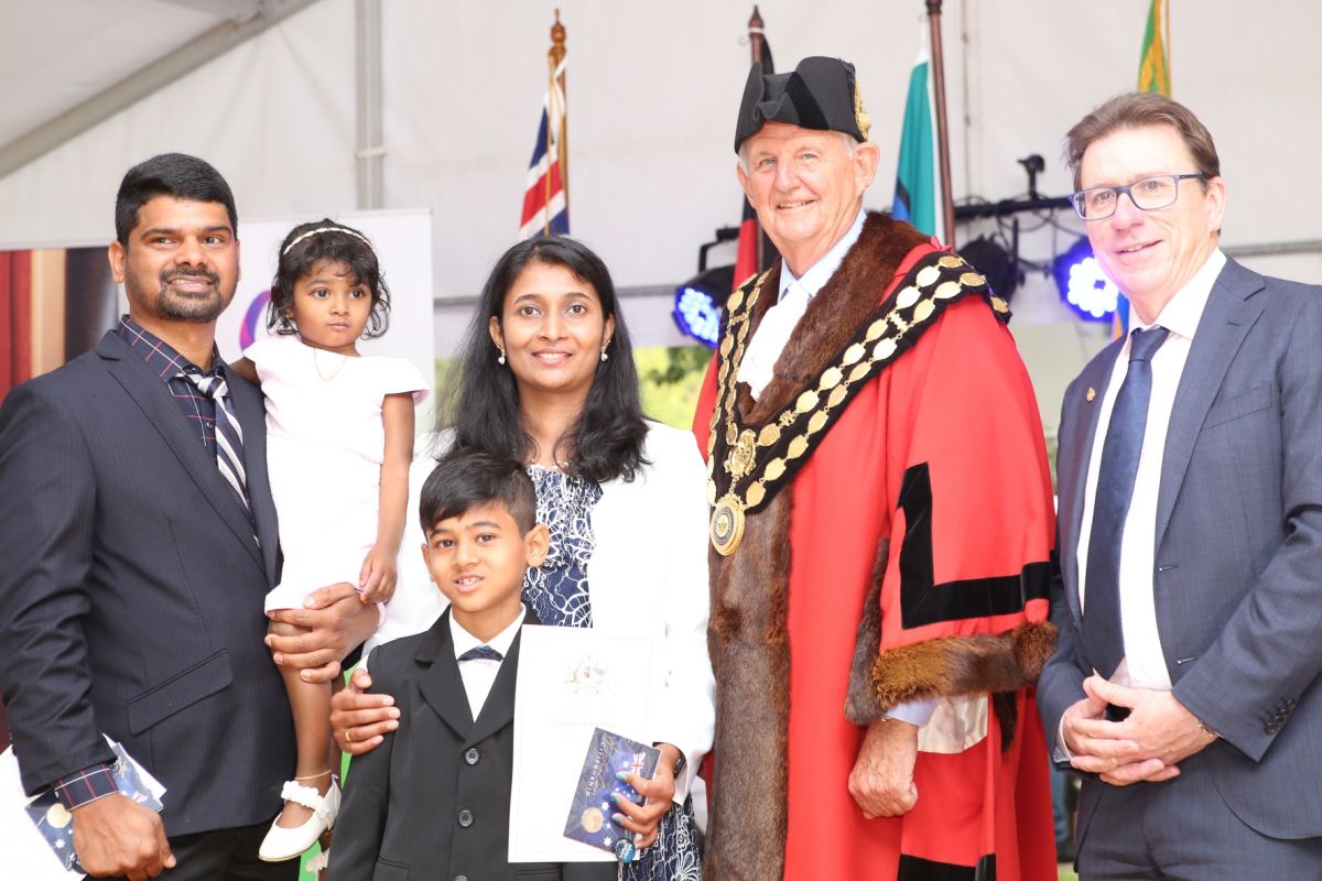 Family with father, mother, two daughters and son holding citzenship certificates, standing next to man in mayoral robes and man in suit