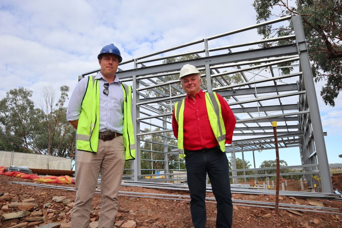 Two men in hi-vis vests standing in front of structural steel frame