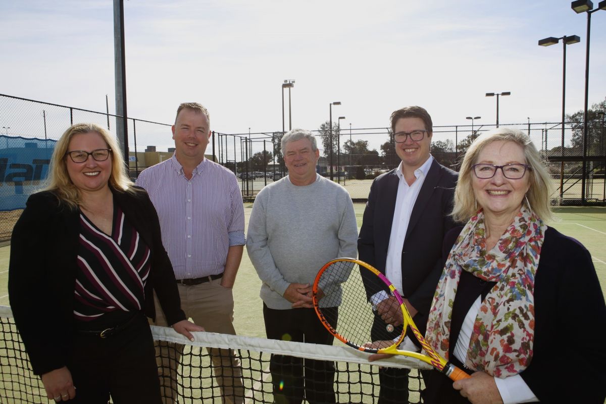 Three men and two women standing around tennis court net
