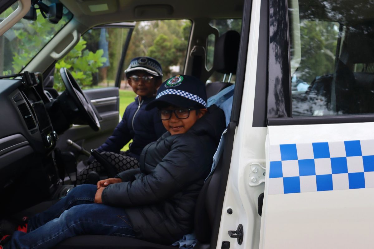 Two girls wearing police caps in front seat of police vehicle