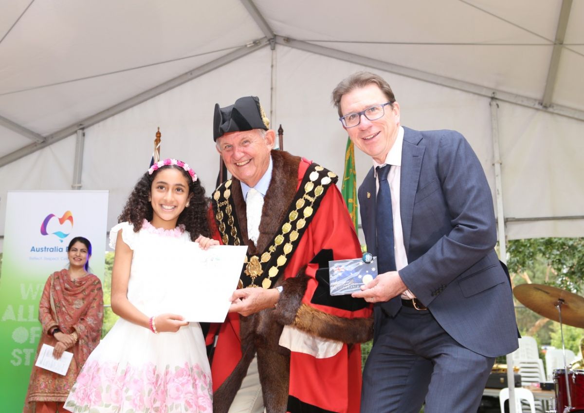 Young girl holding citizenship certificate, standing next to man in mayoral robes and man in suit
