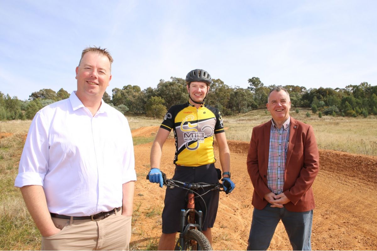 Three men, one holding a bike standing beside mountain bike track