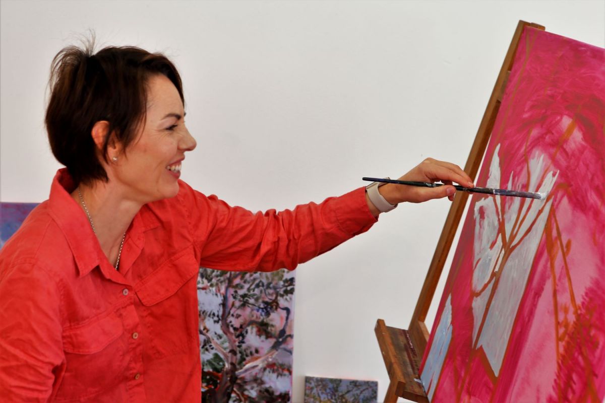 a woman sitting at an easel painting on a canvas