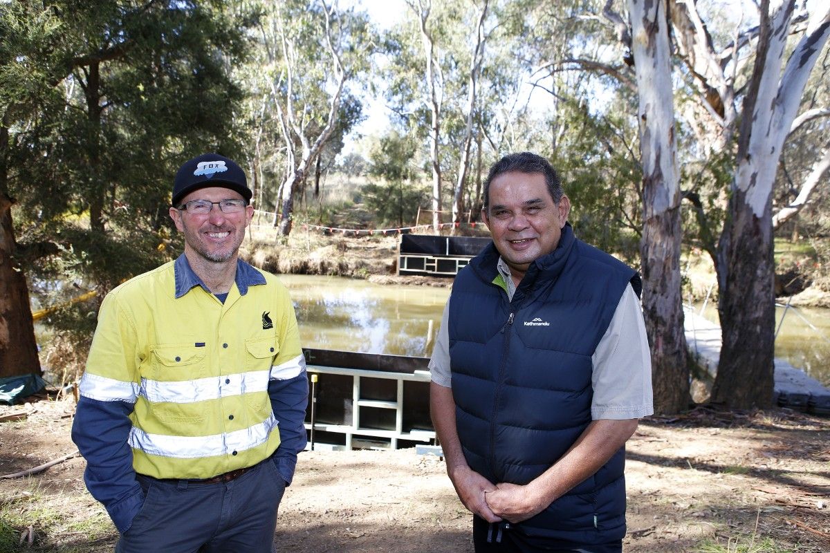 Two men standing next to lagoon anabranch with formwork for new bridge in background