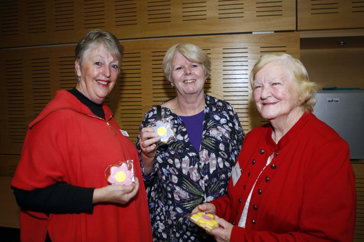 Three ladies inside council meeting room, holding 'thank you' biscuits