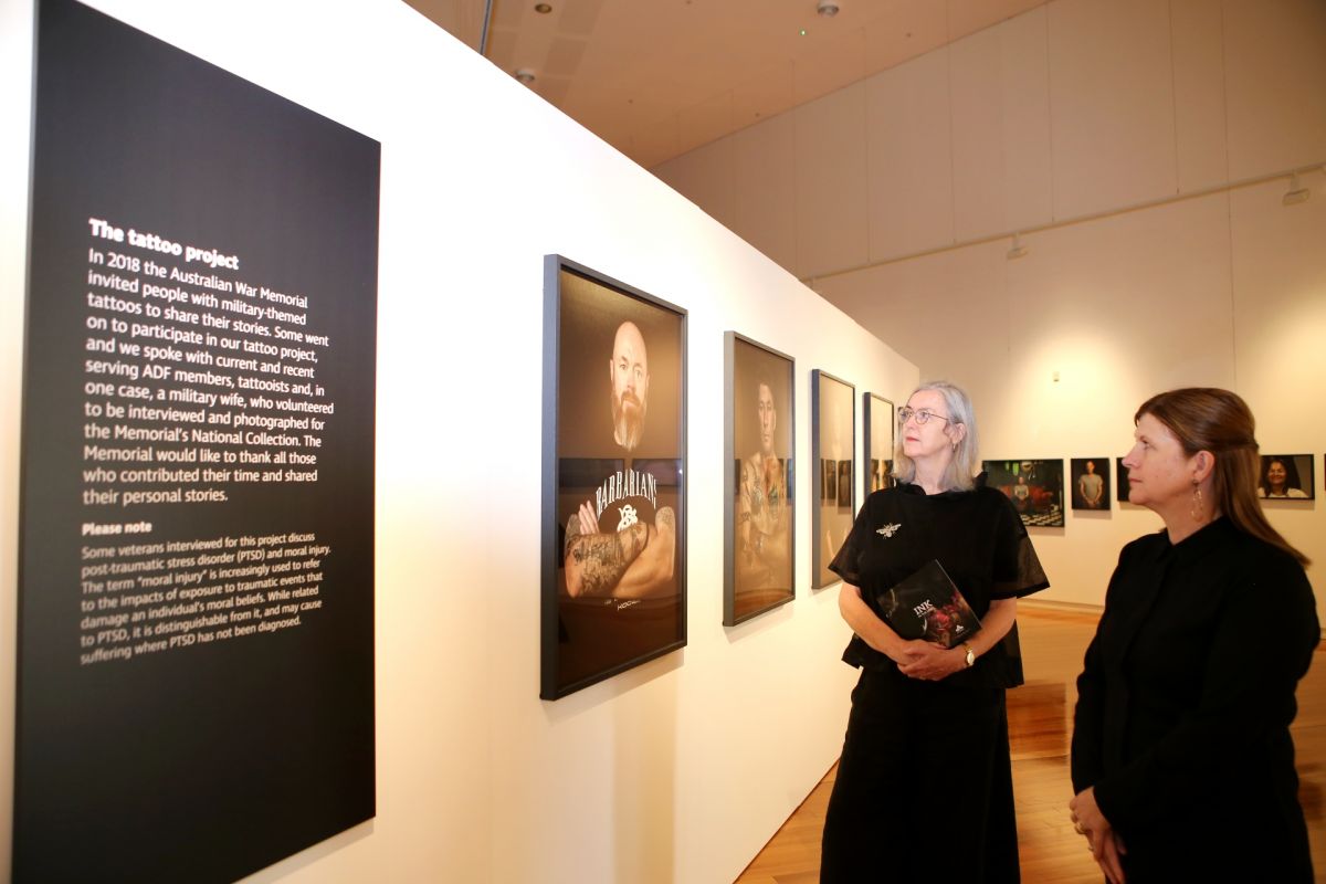 Two women standing next to portraits on gallery wall