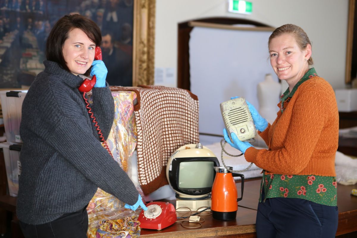 two women standing beside table with 1970s household items