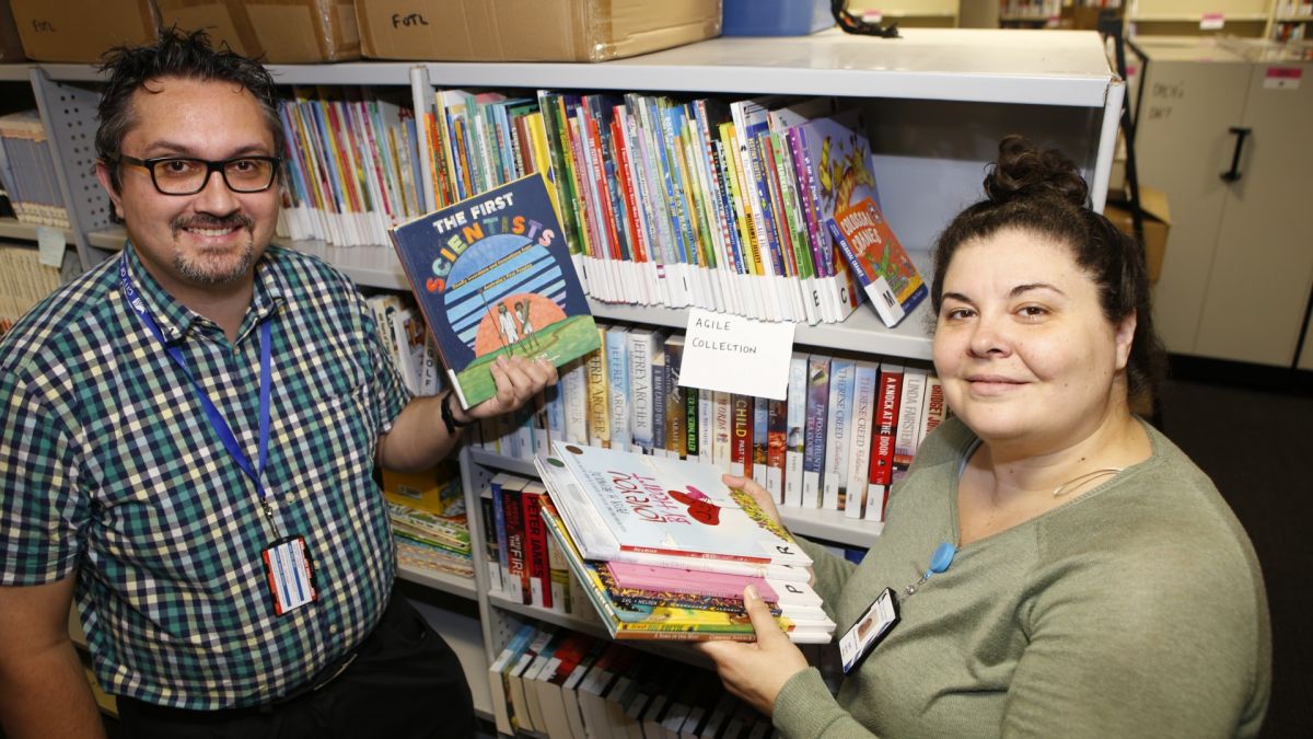Male and female agile library staff standing next to library shelves