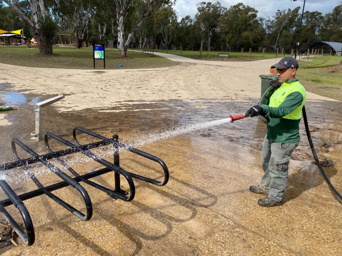 A man hoses down silted pathways