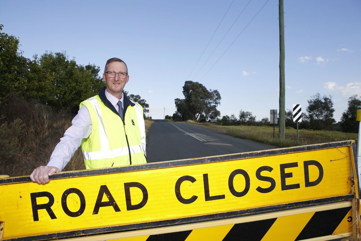 Man in hi-vis vest standing behind road closed sign 